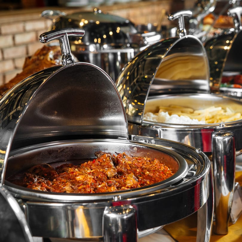 Indian buffet with chicken curry and rice in stainless steel chafing dishes.